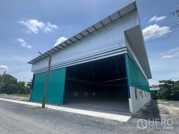 Warehouse for rent in Min Buri, Bangkok - Angled exterior showing a large open warehouse entrance and covered loading area with overhead power lines.