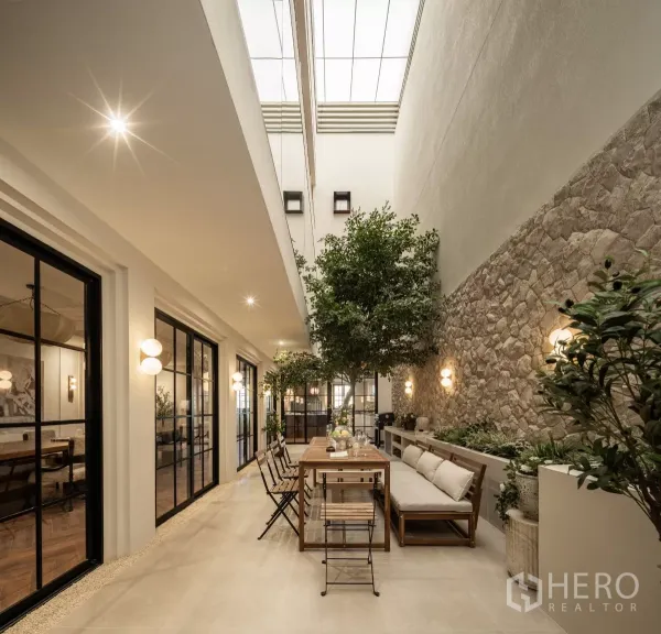 带办公室的家 出售在Phra Khanong, Bangkok - 采光天窗的室内庭院，石质景墙、绿树与长餐桌。