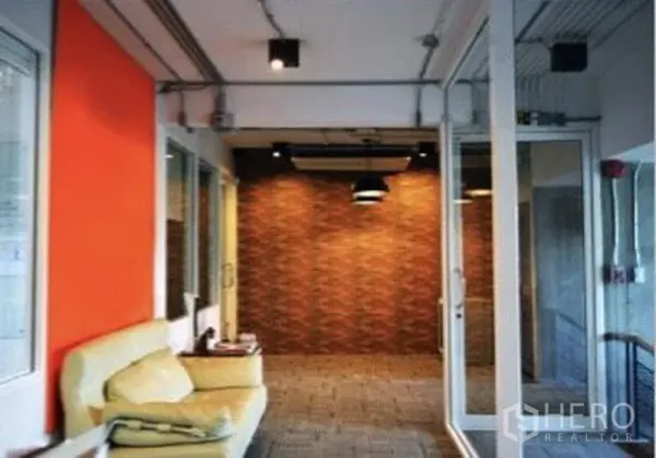 店屋 出租在Suan Luang, Bangkok - 楼层走廊，玻璃隔间与橙色重点墙，沙发休憩区，外露管线与砖纹背景墙。