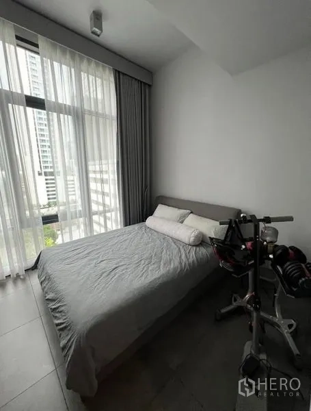 Condominium for rent in Watthana, Bangkok - Second bedroom with large window, bed and home gym equipment.