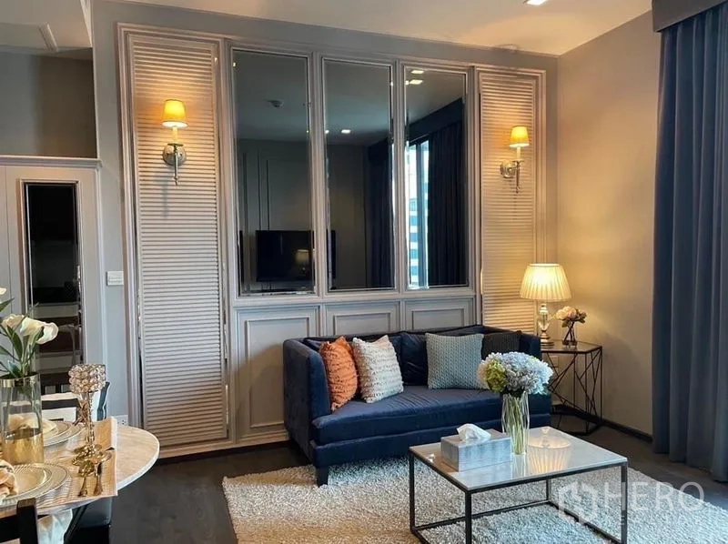 คอนโด ให้เช่าหรือขายในWatthana, Bangkok - ห้องนั่งเล่นมีกระจกเงาบนผนัง โซฟาสีน้ำเงิน และโคมไฟข้างผ้าม่านสูงจรดเพดาน