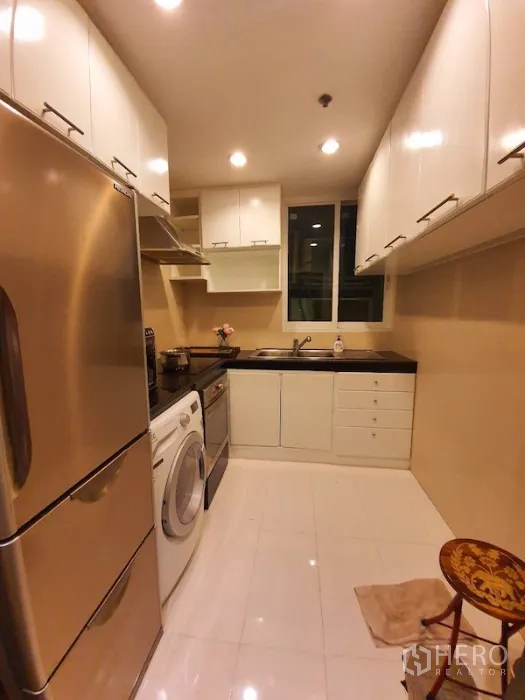 Condominium for rent or sale in Pathum Wan, Bangkok - Galley kitchen featuring white cabinetry, black countertops, stainless fridge, washing machine and a window.