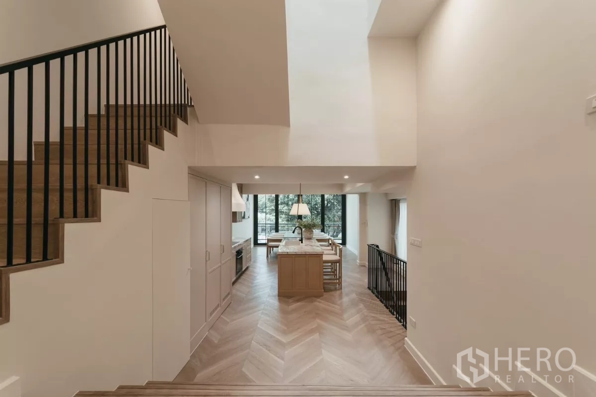 联排别墅 出租在Watthana, Bangkok - 错层走廊通向挑高厨房与餐厅，配落地玻璃门。