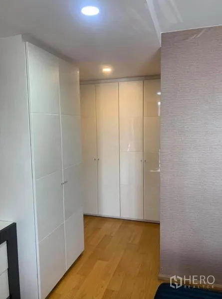 Condominium for rent or sale in Pathum Wan, Bangkok - Hallway lined with glossy white wardrobes and warm wood flooring.