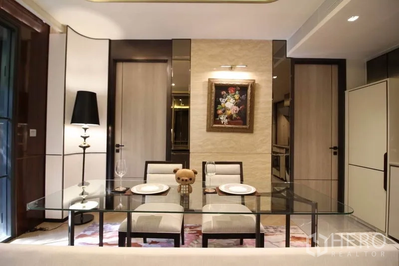 Condominium for rent in Watthana, Bangkok - Close-up of dining space featuring a glass table, upholstered chairs and wall art under soft lighting.