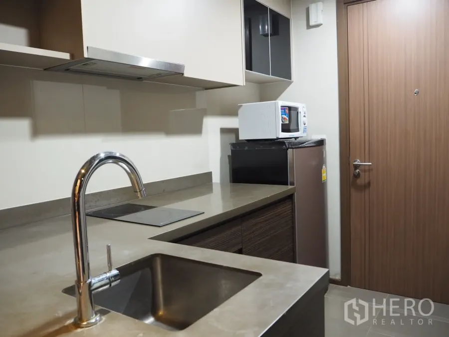 Condominium for rent in Phaya Thai, Bangkok - Compact modern kitchenette with stainless sink, electric cooktop, microwave and fridge in Phaya Thai condo.