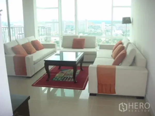 Condominium for rent or sale in Watthana, Bangkok - Bright living room with white sofas, orange cushions, glass coffee table and floor-to-ceiling windows with Bangkok city view.
