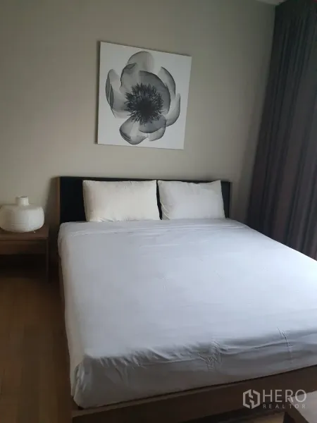 Condominium for rent or sale in Watthana, Bangkok - Master bedroom with a large bed, neutral decor, bedside table and floral wall art.