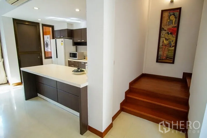 Townhouse for rent in Watthana, Bangkok - Kitchen island with white countertop beside staircase and pantry area.