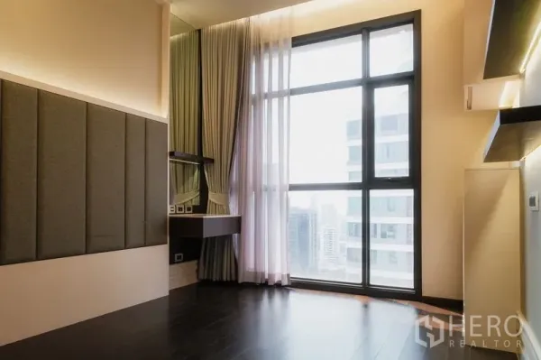 Condominium for rent or sale in Watthana, Bangkok - Bedroom with tall window, study nook and city views through sheer curtains.