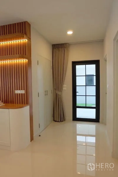Detached House for rent in Bang Phli, Samut Prakan - Hallway with glass back door, built-in storage and a vertical wood feature wall.