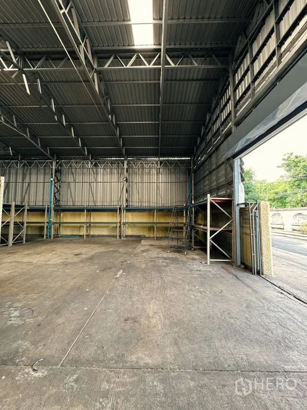 Warehouse for rent in Din Daeng, Bangkok - Inside the warehouse looking toward the open shutter door with natural light and wall shelving.