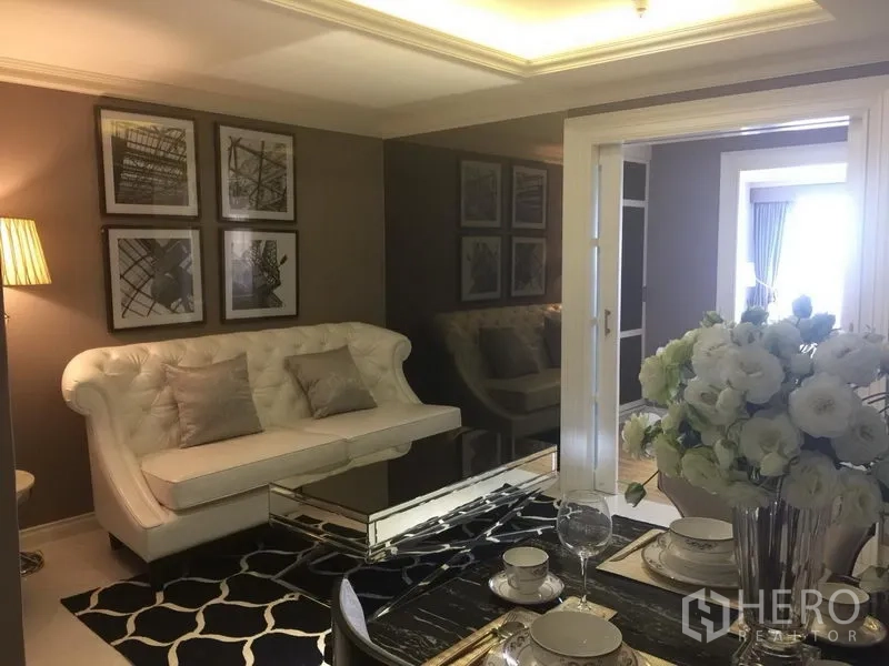 Condominium for rent in Bang Rak, Bangkok - Elegant living and dining room with tufted sofa, wall art, mirror wall and set dining table with flowers.
