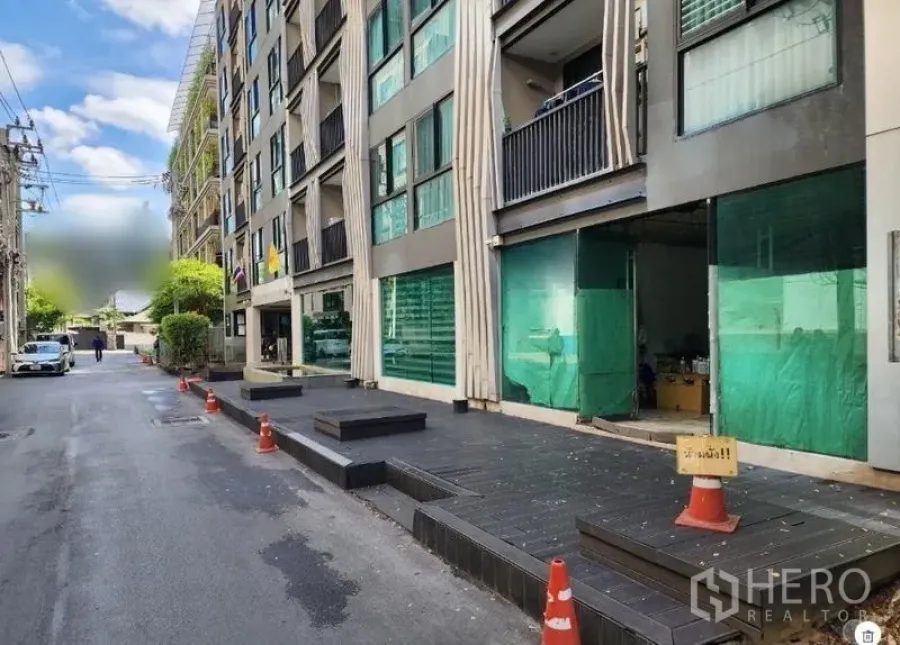 Retail Space for rent - Building frontage along a calm street with cones marking curbside access and multiple shop bays.