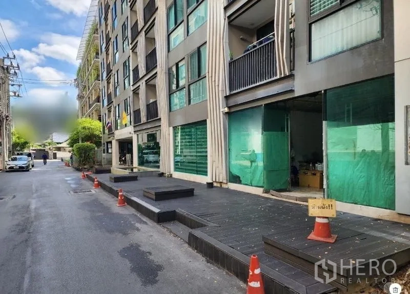 Retail Space for rent - Building frontage along a calm street with cones marking curbside access and multiple shop bays.