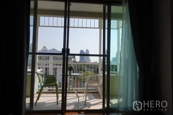 Condominium for rent in Khlong Toei, Bangkok - Balcony seating area with city skyline view through sliding glass doors.