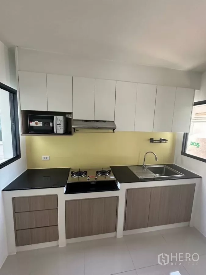 Detached House for rent in Bang Phli, Samut Prakan - Compact modern kitchen with gas hob, range hood, microwave and ample cabinetry.