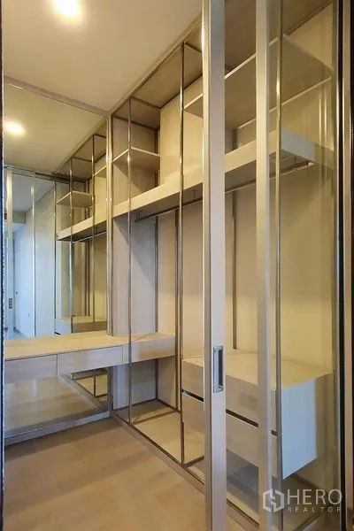 Condominium for sale in Khlong Toei, Bangkok - Walk-in closet with glass doors, built-in shelves, drawers and a vanity with mirrors.