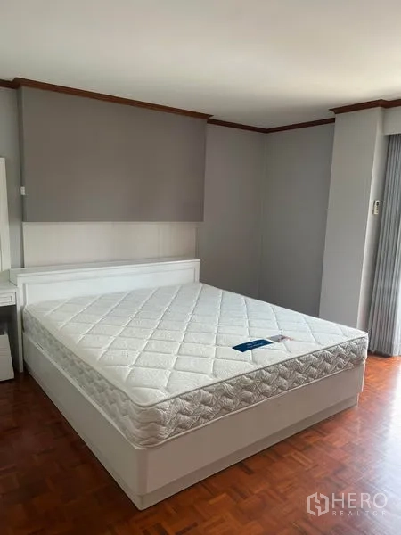 Condominium for rent in Watthana, Bangkok - Spacious master bedroom with large bed, warm wood flooring and soft gray walls.