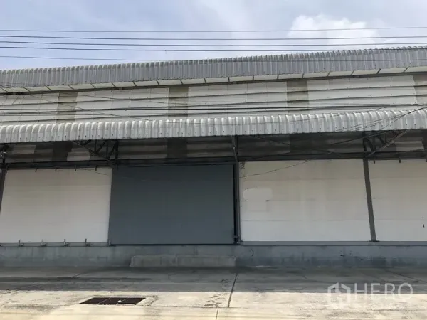 货栈 出租在Khlong Luang, Pathum Thani - 仓库外立面，带雨棚的装卸区、卷帘门与宽阔混凝土场地
