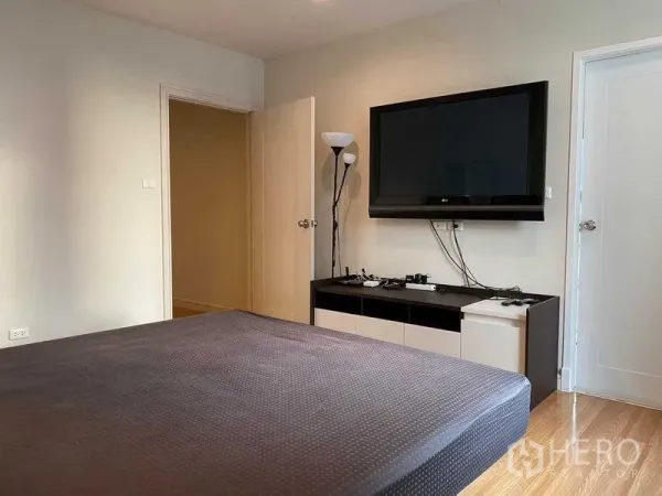 Condominium for rent in Pathum Wan, Bangkok - Bedroom with wall-mounted TV, large bed and warm wood flooring.