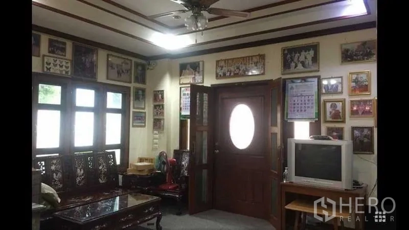 บ้าน ขายในBang Na, Bangkok - ห้องนั่งเล่นสไตล์ดั้งเดิม หน้าต่างกรอบไม้ พัดลมติดเพดาน และตู้ทีวี