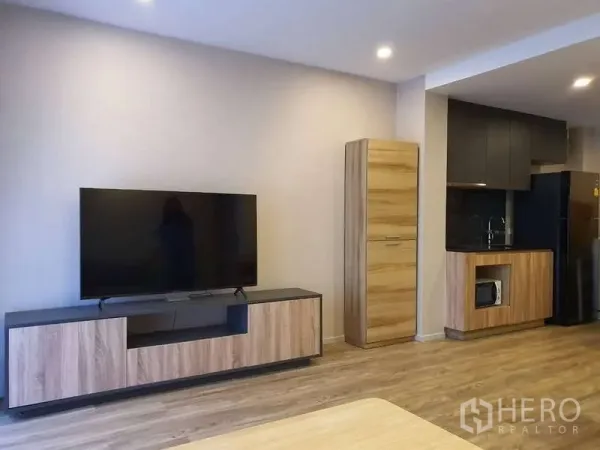 Condominium for rent in Sathon, Bangkok - Open-plan living area with TV unit and pantry kitchen featuring wood cabinetry.