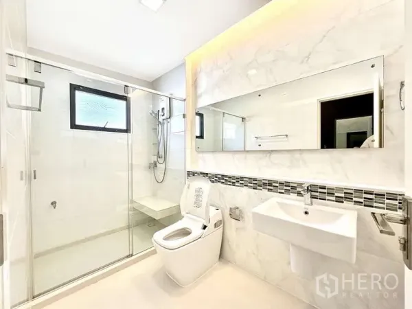 Detached House for sale in Bang Phli, Samut Prakan - Bright bathroom with glass-enclosed shower, large wall mirror and marble-look tiles.