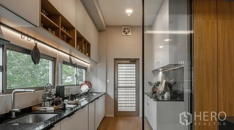 Detached House for rent in Saphan Sung, Bangkok - Modern galley kitchen with black granite countertops, windows, and a glass partition.