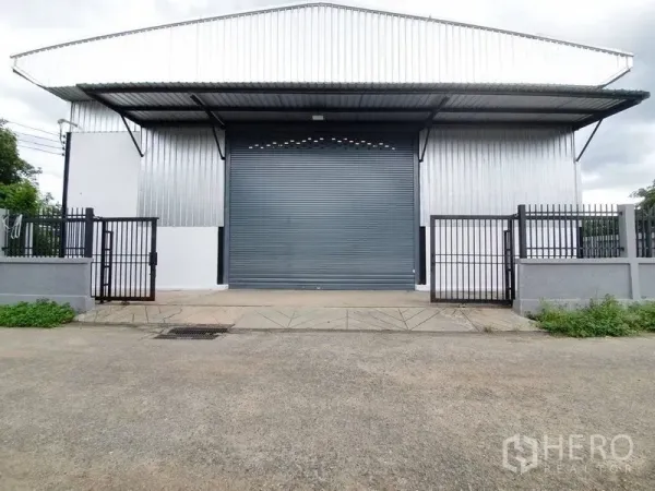 货栈 出租在Bang Khen, Bangkok - 仓库立面对称视角，带装卸坡道、卷闸门与围墙。