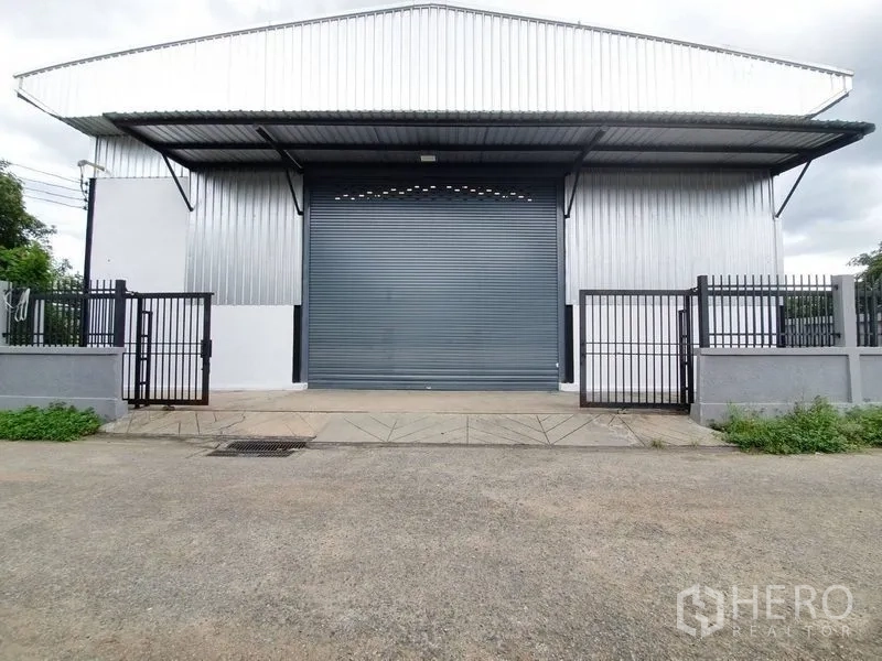 货栈 出租在Bang Khen, Bangkok - 仓库立面对称视角，带装卸坡道、卷闸门与围墙。