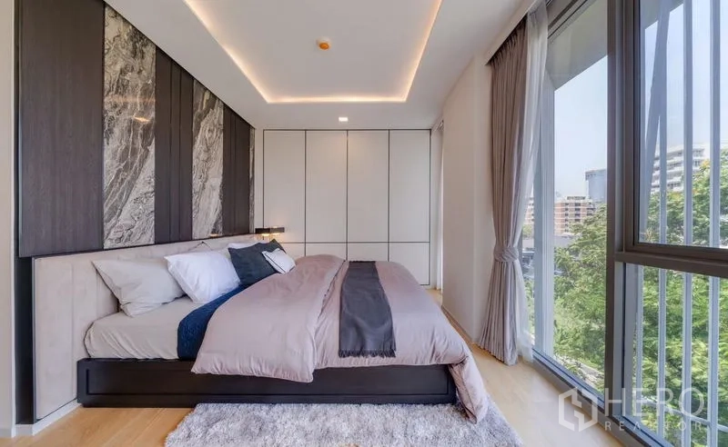 คอนโด ขายในWatthana, Bangkok - ห้องนอนมาสเตอร์สว่างโปร่ง ผนังหัวเตียงลายหินอ่อน ตู้บิลท์อิน และหน้าต่างสูงมองเห็นวิวสีเขียวเมือง