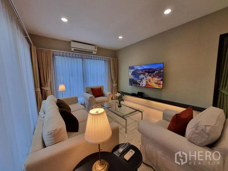Detached House for rent in Bang Khae, Bangkok - Cozy living room with sofa set, glass coffee table, wall-mounted TV, and warm lighting.