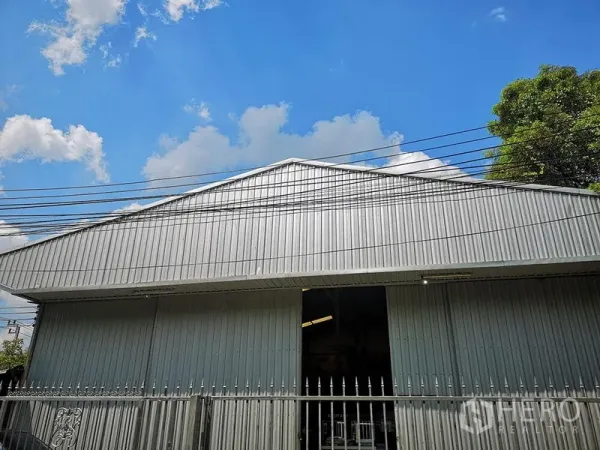 货栈 出租在Bang Khen, Bangkok - 金属壁板仓库的山墙立面，屋顶挑高并有部分开启的入口。