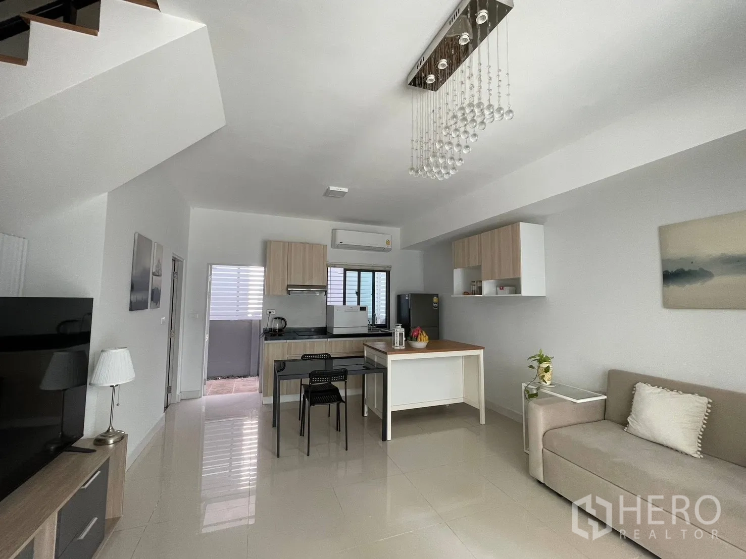 Townhouse for rent in Bang Phli, Samut Prakan - Spacious living area with chandelier, staircase, modern kitchen, and glossy tile floors.