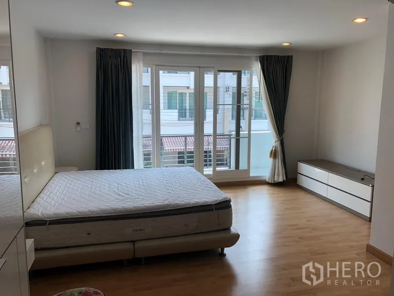 联排别墅 出租或出售在Wang Thonglang, Bangkok - 宽敞卧室，落地窗通向阳台，木地板与低柜储物。