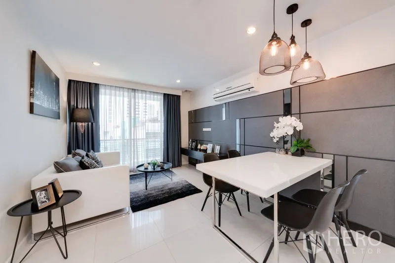 Condominium for sale in Bang Rak, Bangkok - Bright open-plan living and dining area with white sofa, pendant lights, and floor-to-ceiling windows in a modern Bangkok condo.