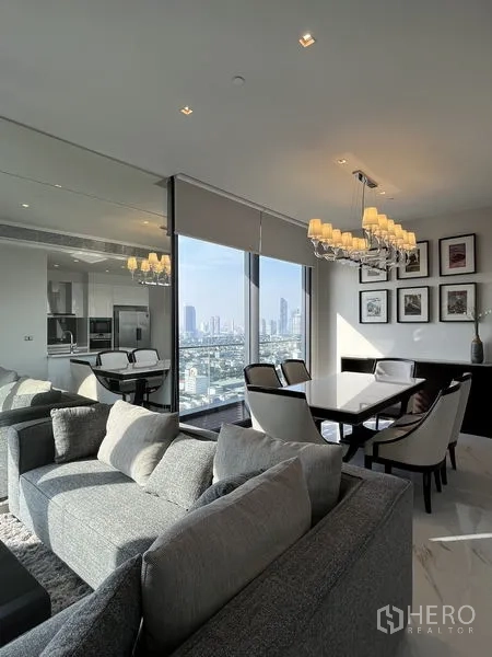 Condominium for rent or sale in Bangkok - Furnished living-dining space with chandelier, sofa set and large windows showcasing city views.
