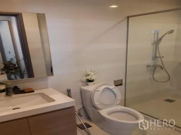 Condominium for rent in Khlong Toei, Bangkok - Modern bathroom with vanity, toilet, and a glass-enclosed shower.