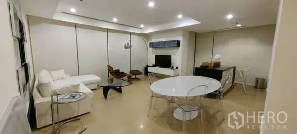 Condominium for rent in Khlong San, Bangkok - Open-plan living and dining room in a Bangkok condo with white sofa, round table, TV wall and recessed lighting.