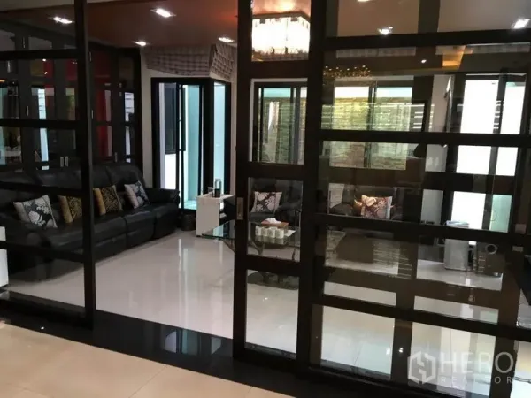Detached House for rent in Khlong Toei, Bangkok - Glass-partitioned sitting area with black leather sofas and glossy tiled floor.