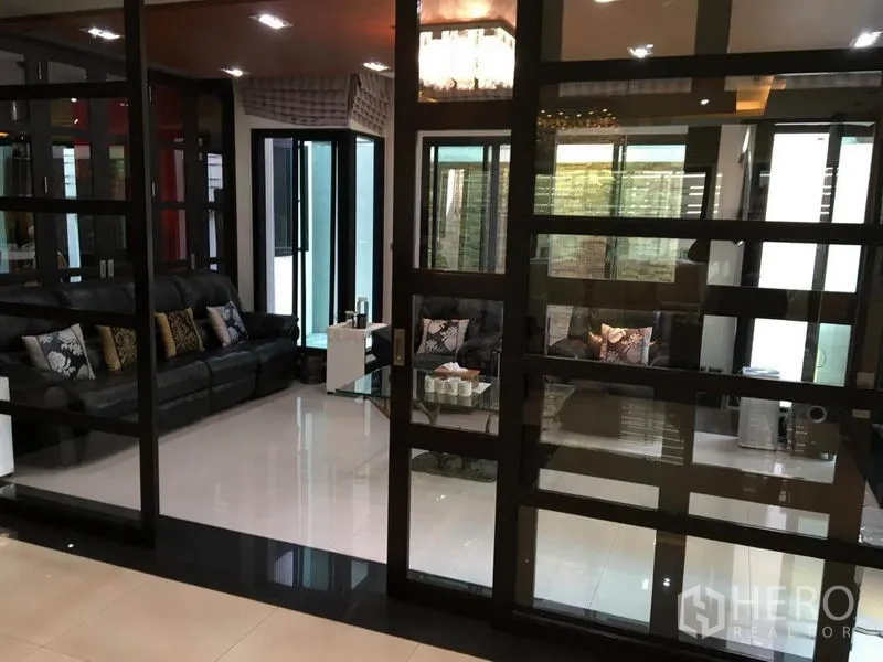 Detached House for rent in Khlong Toei, Bangkok - Glass-partitioned sitting area with black leather sofas and glossy tiled floor.