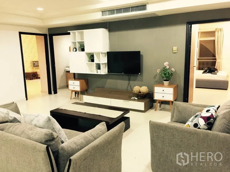 Condominium for rent or sale in Watthana, Bangkok - Modern lounge with TV feature wall, decorative shelving and doorway to a bedroom.