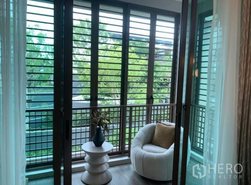 独立式住宅 出售在Bang Kapi, Bangkok - 二层阳台带百叶遮阳，单人沙发与绿树景致，通风良好。