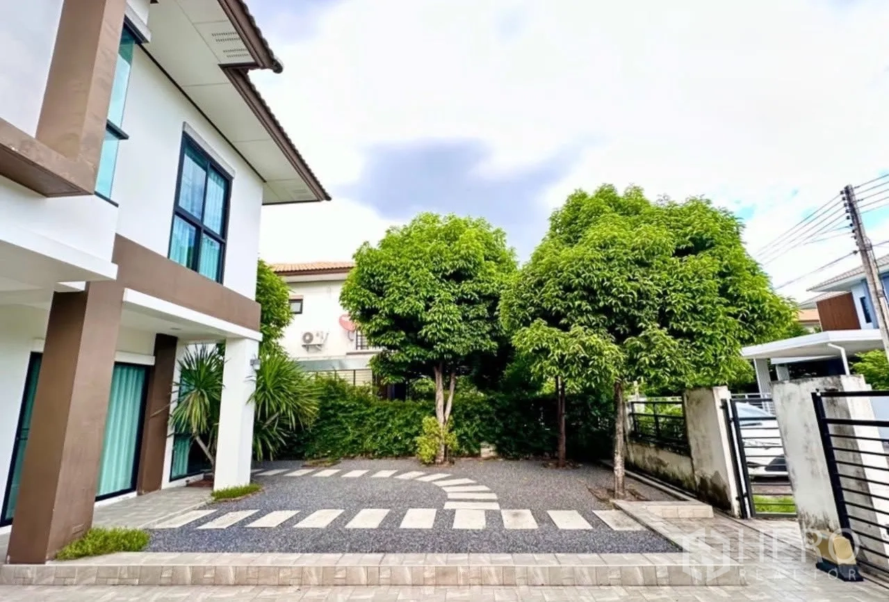 บ้าน ขายในLam Luk Ka, Pathum Thani - ลานหน้าบ้านมีทางรถ ก้อนทางเดิน และต้นไม้ให้ร่มเงาใกล้ประตูรั้ว