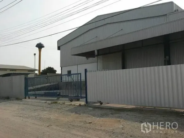 货栈 出租在Chon Buri - 仓库外立面与围栏滑动门，临宽阔道路，可见水塔