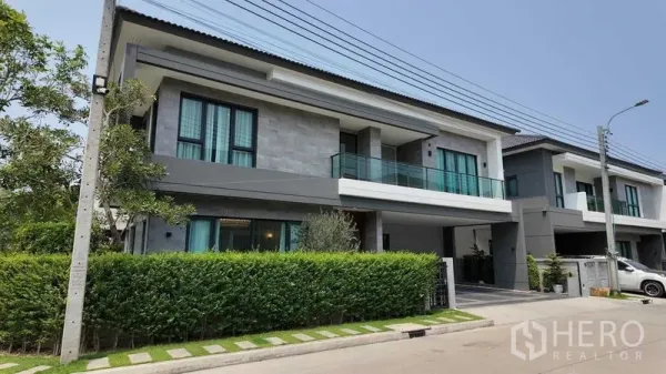 Detached House for rent or sale in Bang Na, Bangkok - Street‑facing exterior of the modern detached house with hedge fence and balcony.