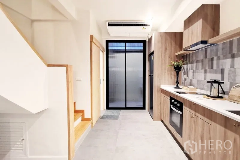 联排别墅 出租在Khlong Toei, Bangkok - 走廊式厨房，内置家电、空调与通向生活阳台的玻璃门。