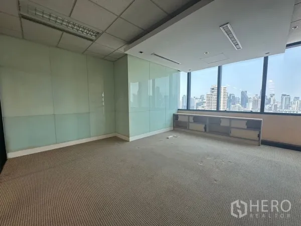 Office Space for rent in Khlong Toei, Bangkok - Corner office with frosted glass wall panels, built-in shelf, and panoramic skyline through large windows.