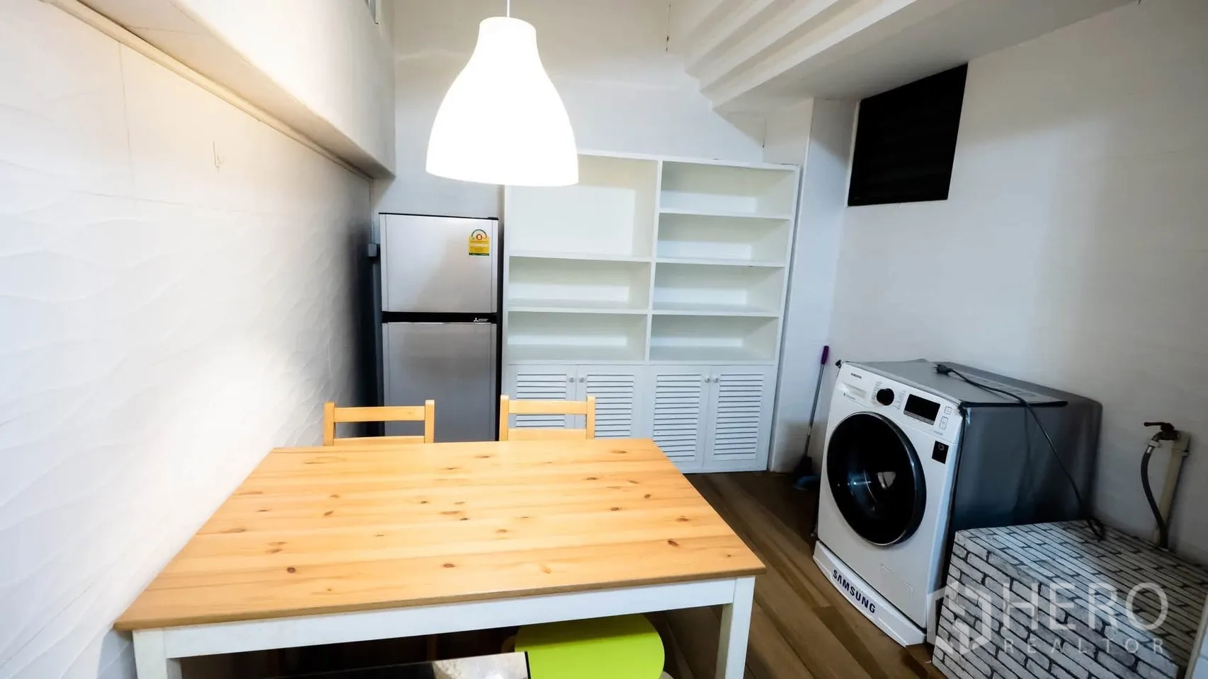 Townhouse for rent in Watthana, Bangkok - Dining nook with wooden table, refrigerator, shelving, and a washing machine.